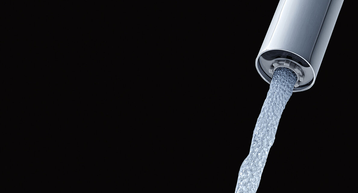 Primo piano dell'uscita di un rubinetto con ECOCAP su sfondo nero. Il getto d'acqua che esce dal rubinetto è intervallato da piccole bolle d'aria.