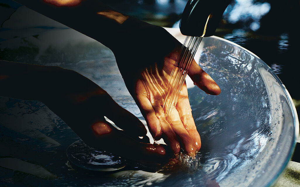 This picture shows a washbasin with a TOTO tap above it. Several small jets of water come out of the faucet spout. A hand is held under these jets of water.