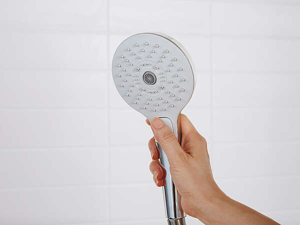 One hand holds up a TOTO shower head. The shower head is switched off.