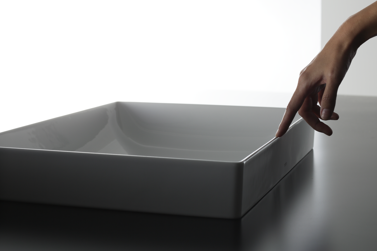 This picture shows a washbasin. The washbasin is located on a vanity unit. A hand runs its finger over the edge of the washbasin.