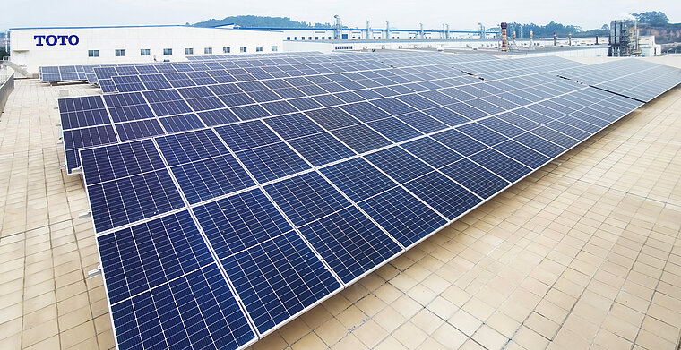The photo shows a large array of solar panels on the roof of an industrial building with the TOTO logo in the background.