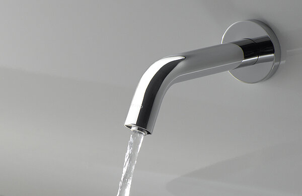 Eine Armatur ist an einer Wand über einem Waschtisch angebracht. Die Armatur ist eingeschaltet und aus ihr kommt ein Wasserstrahl. 